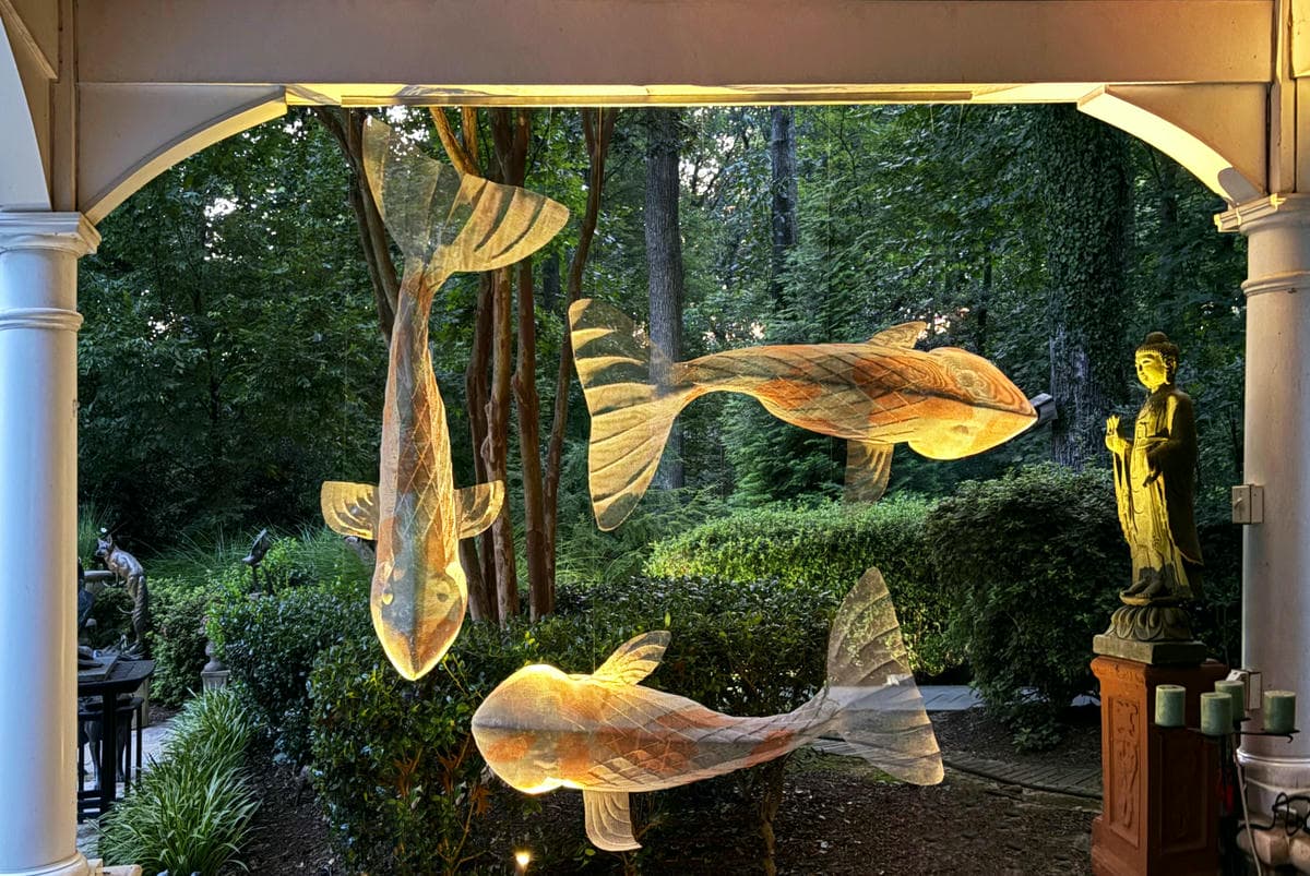 Three suspended fish sculptures are positioned in a garden pavilion - artwork by sculptor David Begbie